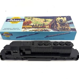 May include: A black Athearn HO scale model train locomotive with a detailed design. The model is next to its blue box, which features a train scene. The box reads "Authentic-Realistic" and "Miniature".