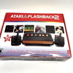 May include: Atari Flashback 2 Classic Game Console box. The box is red and black with the Atari logo and the words "Flashback 2". The console is black and orange, with two joysticks. The box says "40 Built-in Games".