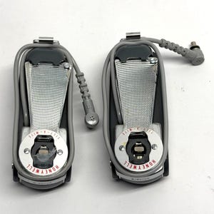 May include: Two gray Honeywell Fill-A-Mite devices with silver and black accents. Each device has a silver strap and a circular base with the Honeywell logo. One device has a gray cord attached.
