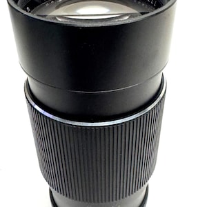 May include: A black Bushnell camera lens with the text "Bushnell" and "No. 711635" visible. The lens has a ribbed grip and measurement markings. The words "Made in Japan" are also visible.