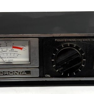 May include: Black Micronta field strength/SWR tester with a gauge, dial, and switch. The gauge reads power and field strength. The text "Micronta" is visible on the front. The device has a FS ANT connector.