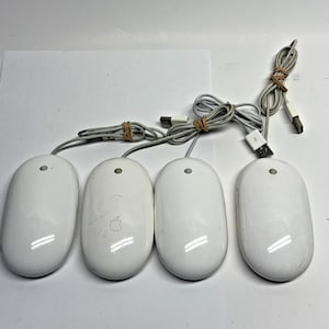May include: Four white Apple computer mice with attached gray cords and USB connectors. The mice are oval-shaped with a single button and a small circular indentation. The cords are bundled with rubber bands.