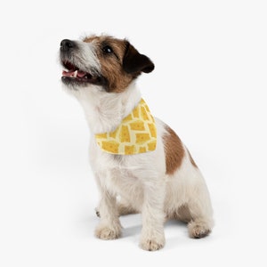 May include: A white and brown Jack Russell Terrier dog wearing a yellow bandana with a cheese pattern. The dog is sitting and looking up.