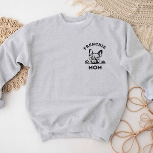 May include: Gray sweatshirt with a black graphic of a French bulldog peeking out of a box with the text "Frenchie Mom".