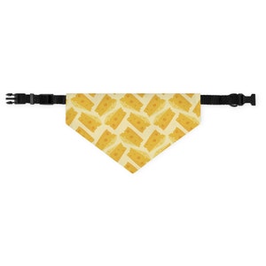 May include: A yellow and white dog bandana with a pattern of cheese slices. The bandana has black adjustable straps.