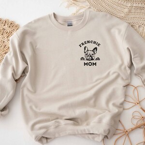 May include: Beige sweatshirt with a black graphic of a French bulldog peeking over the top of the text "Frenchie Mom".