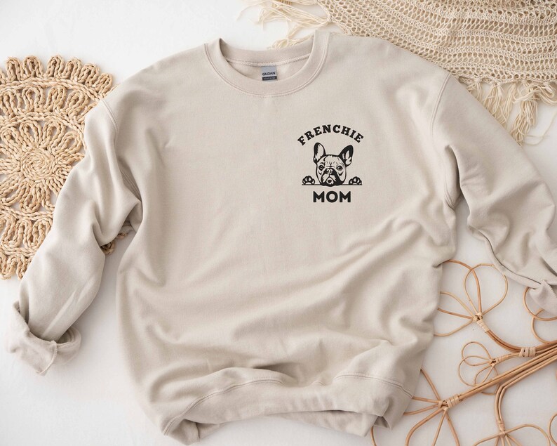 May include: Beige sweatshirt with a black graphic of a French bulldog peeking over the top of the text "Frenchie Mom".