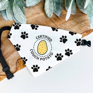 Puede incluir: Bandana blanca para perros con huellas de patas negras y la frase "CERTIFIED COUCH POTATO" alrededor de una ilustraci&oacute;n de patata amarilla. Tiene una correa y hebilla negras ajustables.
