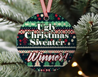 以下が含まれることがあります： 赤いリボンが付いた丸いクリスマスオーナメントで、白と赤で「Ugly Christmas Sweater Winner！」の文字が書かれています。オーナメントは、赤、緑、白のお祝いのデザインのパターンを持つ濃い青緑色の背景を持っています。