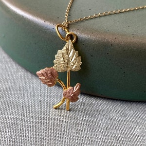 May include: A gold necklace with a pendant featuring three leaves in a cluster. The leaves are made of gold and rose gold.