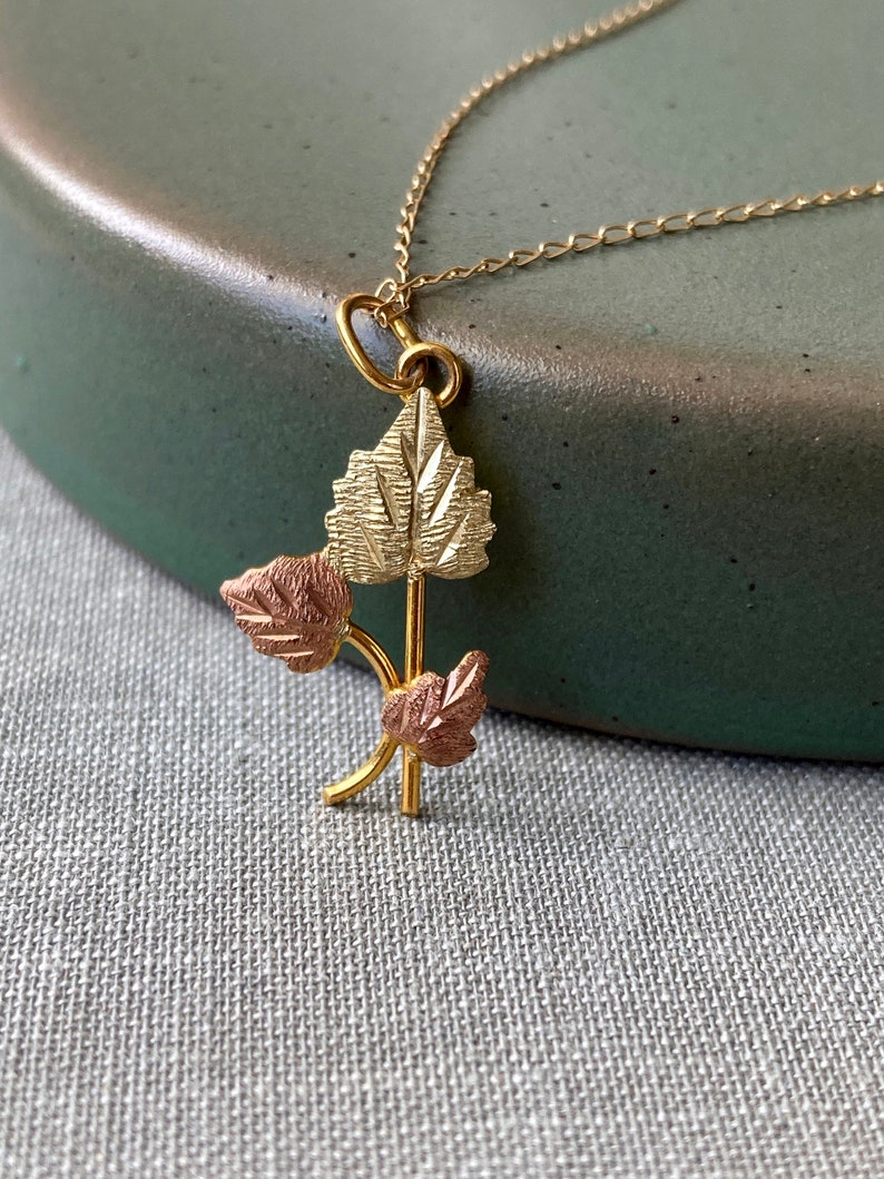 May include: A gold necklace with a pendant featuring three leaves in a cluster. The leaves are made of gold and rose gold.