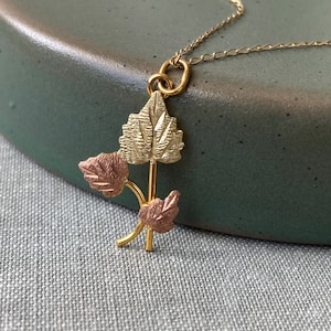 May include: A gold necklace with a pendant featuring three leaves. The leaves are made of gold and rose gold.