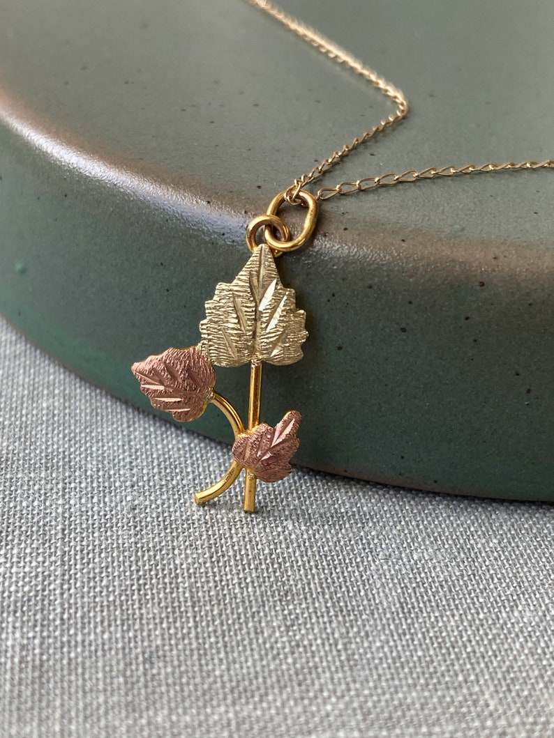 May include: A gold necklace with a pendant featuring three leaves. The leaves are made of gold and rose gold.