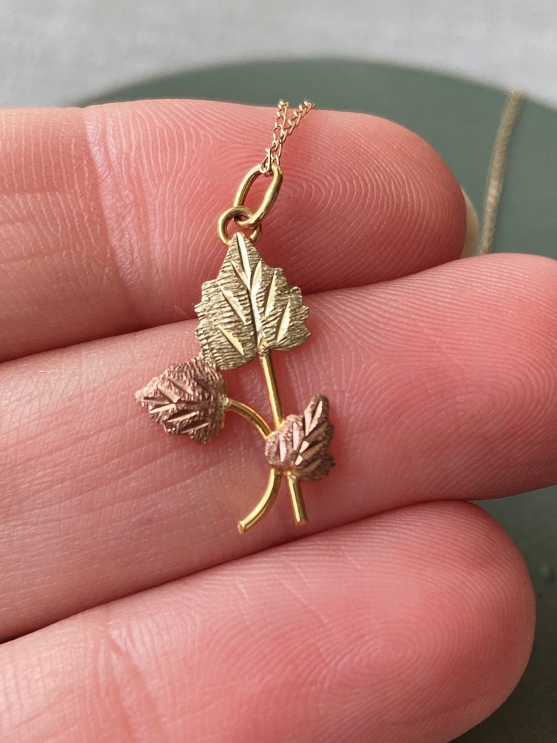 May include: A gold necklace with a pendant featuring three leaves in a cluster. The leaves are made of gold and have a textured surface. The necklace is on a chain.