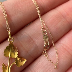 May include: A gold chain necklace with a delicate leaf pendant. The pendant features three leaves connected by a stem. The chain is a delicate, fine link chain. The pendant has the number "10" stamped on the back.