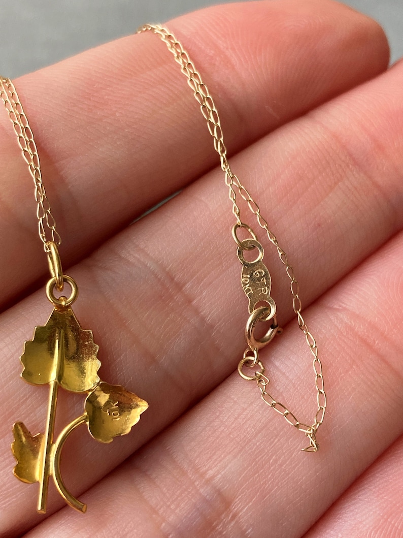 May include: A gold chain necklace with a delicate leaf pendant. The pendant features three leaves connected by a stem. The chain is a delicate, fine link chain. The pendant has the number "10" stamped on the back.