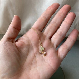May include: A gold necklace with a pendant featuring three leaves in shades of green and pink.