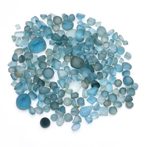 May include: A scattering of blue-green gemstones in various shapes, including round, oval, and faceted cuts. The gemstones are displayed on a white background, with a range of light to dark blue hues. The image presents a collection of natural gemstones.