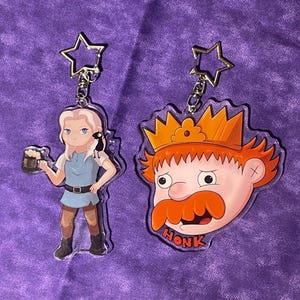 Peut inclure: Deux porte-clés de personnages, l'un représentant une femme de dessin animé tenant une chope de bière et l'autre un homme de dessin animé avec une couronne et le mot "HONK" imprimé en dessous.