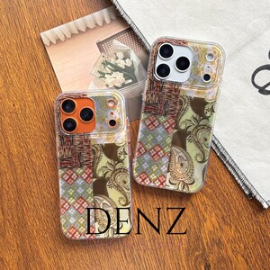 May include: Two clear phone cases with a patchwork design. The cases feature a mix of patterns, including paisley and geometric shapes, in shades of brown, red, and green. The word "DENZ" is printed in gold at the bottom of one case.