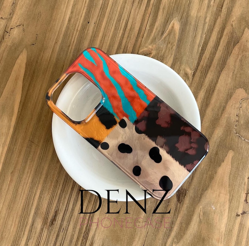 May include: A patterned phone case with a patchwork design. The case features sections of orange, teal, and brown animal print patterns. The brand name "DENZ PHONE CASE" is printed at the bottom of the case.