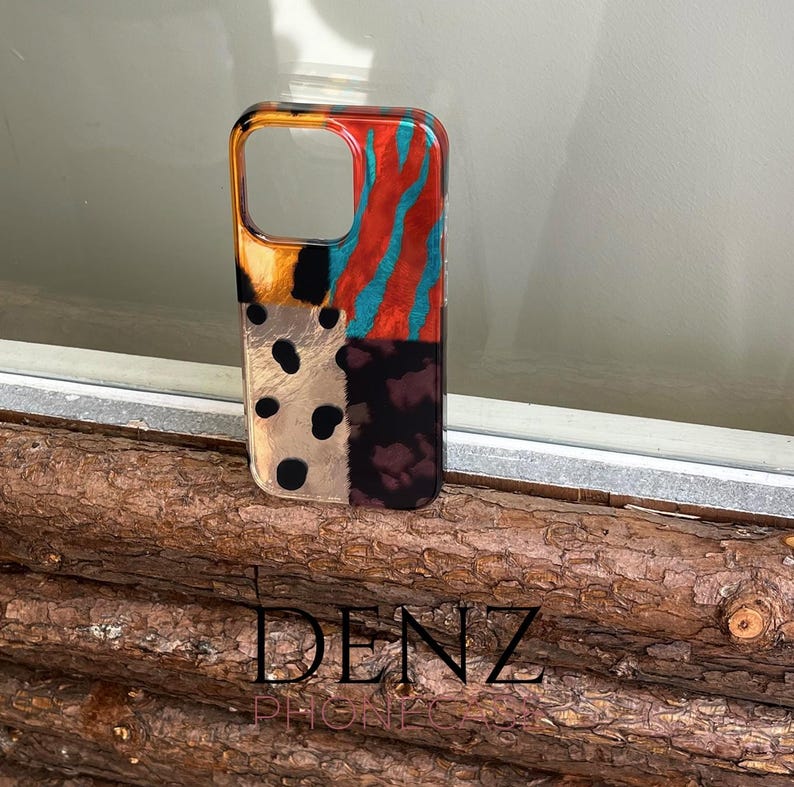 May include: A patterned phone case in a vibrant design. The case combines animal print, stripes, and polka dots in orange, teal, black, and brown. The brand name "DENZ PHONES" is printed at the bottom. A stylish accessory for a mobile phone.