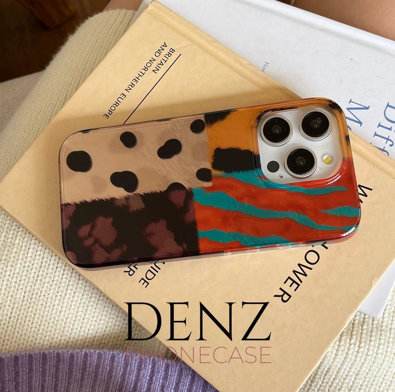 May include: A patterned phone case with a clear border. The case has sections with leopard print, a dark maroon pattern, orange and teal stripes. The text "DENZ" and "ONECASE" are visible on the book below the phone case.