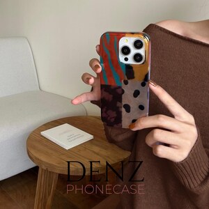 May include: A patterned phone case with a vibrant patchwork design. The case displays sections of red and teal stripes, yellow, brown, and black polka dots. The brand name "DENZ PHONECASE" is printed at the bottom.