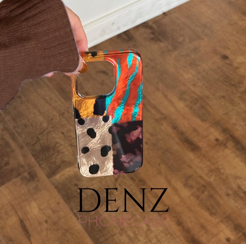 May include: A clear phone case with a vibrant abstract design. The case displays a patchwork of patterns in orange, teal, black, and gold. The text "DENZ" is printed at the bottom of the case.