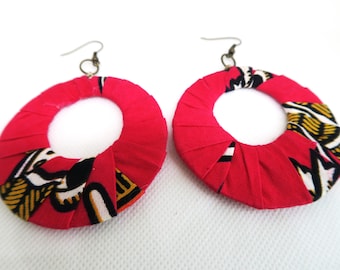 May include: A pair of large, round hoop earrings made from fabric. The earrings are red with a black, white, and gold patterned design.