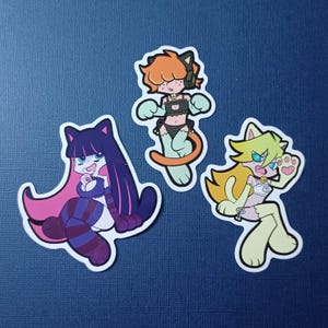 Può includere: Tre adesivi di cartoni animati con personaggi in stile anime con disegni a tema gatto. Gli adesivi mostrano personaggi con orecchie, code e abiti da gatto in vari colori, tra cui rosa, viola, arancione e giallo. Ogni adesivo ha un bordo bianco.