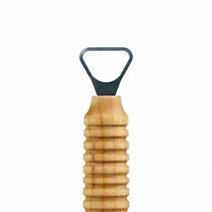 Puede incluir: Un abridor de botellas de madera con un abridor de metal gris oscuro. El mango es de madera de color claro con un diseño acanalado. El abridor está diseñado para abrir botellas.