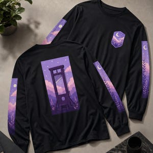 Peut inclure: Un t-shirt noir à manches longues avec un motif de guillotine sur un ciel violet et rose avec des nuages et des étoiles. Les manches présentent des bandes verticales avec un croissant de lune et des feuillages, et un emblème assorti sur la poitrine.