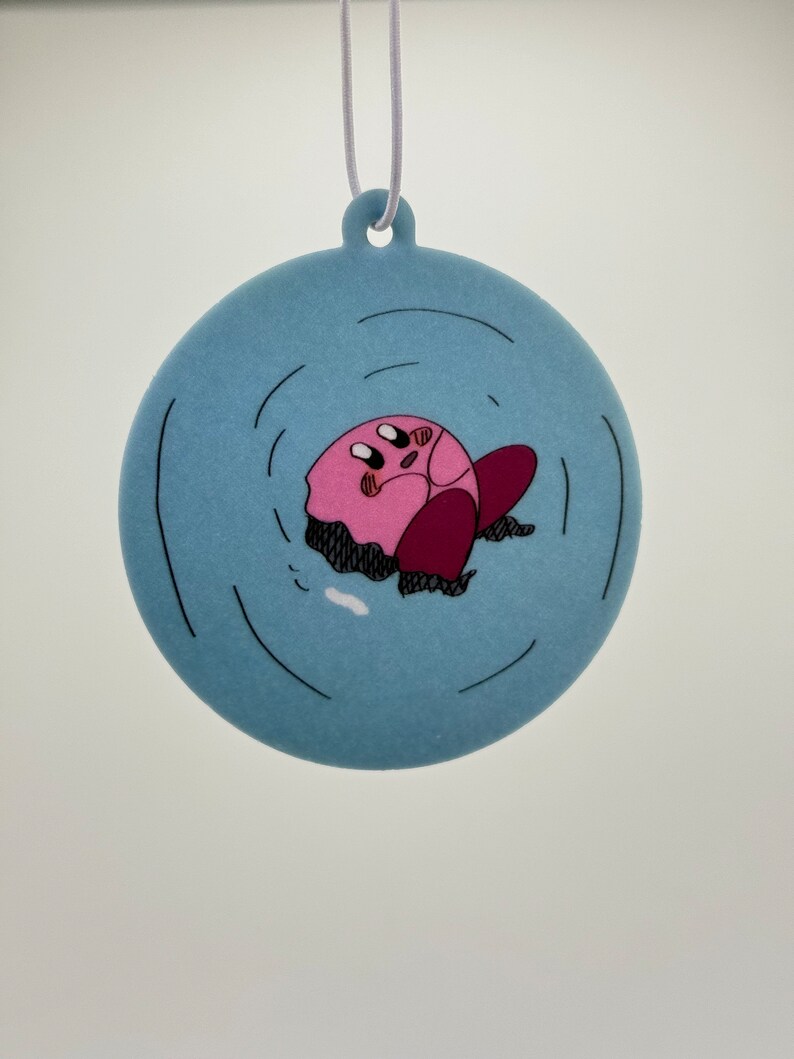 K&ouml;nnte beinhalten: Ein runder blauer und wei&szlig;er Anh&auml;nger mit einer rosa Comicfigur, Kirby, die im Wasser versinkt. Der Anh&auml;nger hat eine wei&szlig;e Schnur zum Aufh&auml;ngen.