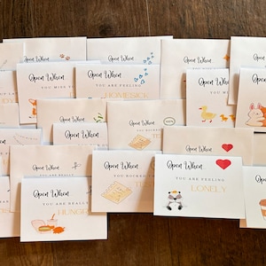 May include: A collection of 20 small white cards with colorful illustrations and text that reads "Open When..." followed by a phrase. The phrases include "You need to make a big decision", "You are really hungry", "You rocked that test", "You are feeling lonely", "You need a hug", and "You need caffeine".