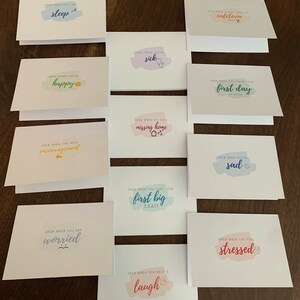 May include: A set of 10 cards with colorful watercolor backgrounds and encouraging messages. The messages include "Open when you can't sleep", "Open when you're happy", "Open when you need encouragement", "Open when you are worried", "Open when you need a laugh", "Open when you're sick", "Open when you are missing home", "Open when you take your first big exam", "Open when you finish your first day of class", and "Open when you feel stressed".