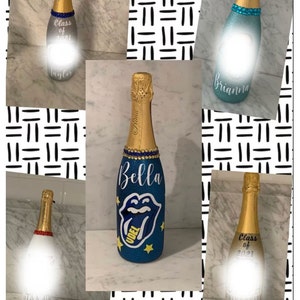 May include: A collage of six personalized champagne bottles decorated with glitter, rhinestones, and paint. The bottles feature names like "Bella", "Brianna", "Taylor", and "John". Some bottles have the text "Class of 2021" and a school logo.