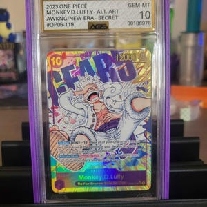 May include: A graded trading card featuring Monkey D. Luffy from One Piece. The card is encased in a purple holder and has the text "2023 ONE PIECE" and "Monkey D. Luffy" visible. The card is graded GEM-MT 10.