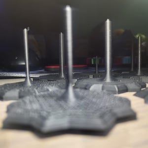 May include: A close-up of several black 3D printed star-shaped bases with tall, thin, black spikes rising from the center of each base.