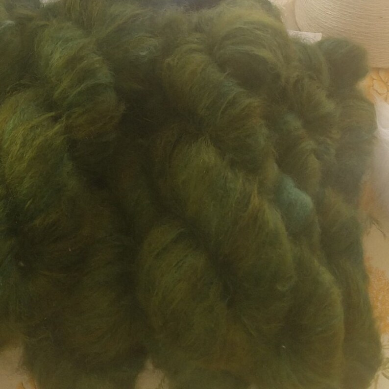 Pu&ograve; includere: Un mucchio di filato verde scuro con una texture leggermente screziata.