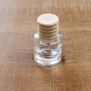 May include: A clear glass bottle with a wooden lid. The lid is made of multiple layers of wood.
