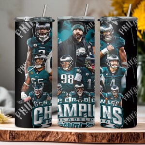 May include: Three stainless steel tumblers featuring Philadelphia Eagles players and the text "Super Bowl Champions". The tumblers have a black background with the team's logo and colors. Each tumbler has a silver straw.