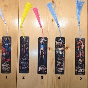 May include: Five rectangular bookmarks with colorful tassels. Each bookmark features a unique design with fantasy themes, including butterflies, dream catchers, dragons, and skulls. Text on the bookmarks includes phrases like "Reading is my Therapy" and "Entering Fantasy."