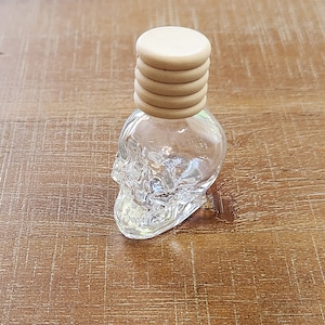 May include: A clear glass bottle shaped like a skull with a wooden lid. The lid is made of four stacked wooden circles.