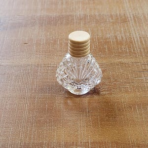May include: A clear glass bottle with a textured surface and a wooden lid. The bottle is shaped like a seashell.