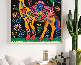 May include: A framed, colorful painting of a camel with floral patterns. The camel is yellow with pink, blue, and red accents, set against a black background filled with flowers. The artwork is displayed in a room with a cactus and a beanbag chair.