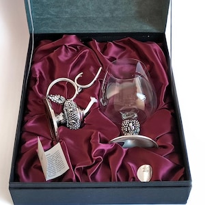 May include: A silver and glass decanter set in a black box with a red satin lining. The box has the text "Farco Gifts" on the lid.