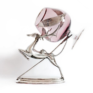 May include: A silver deer figurine with a purple glass decanter on its back. The decanter has a silver chain and a silver base.