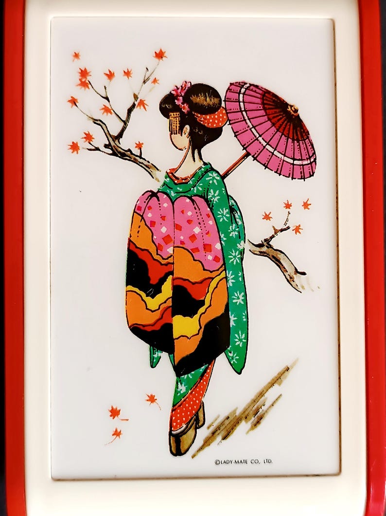 K&ouml;nnte beinhalten: Dekoratives Bild einer Geisha in einem farbenfrohen Kimono, die einen rosa Sonnenschirm h&auml;lt und in der N&auml;he eines Zweigs mit roten Bl&auml;ttern steht. Das Bild ist vor einem wei&szlig;en Hintergrund und rot-wei&szlig; gerahmt.