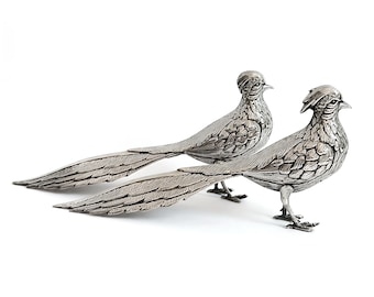 May include: Two silver pheasant figurines with detailed feather patterns. The birds are posed with their tails spread out.